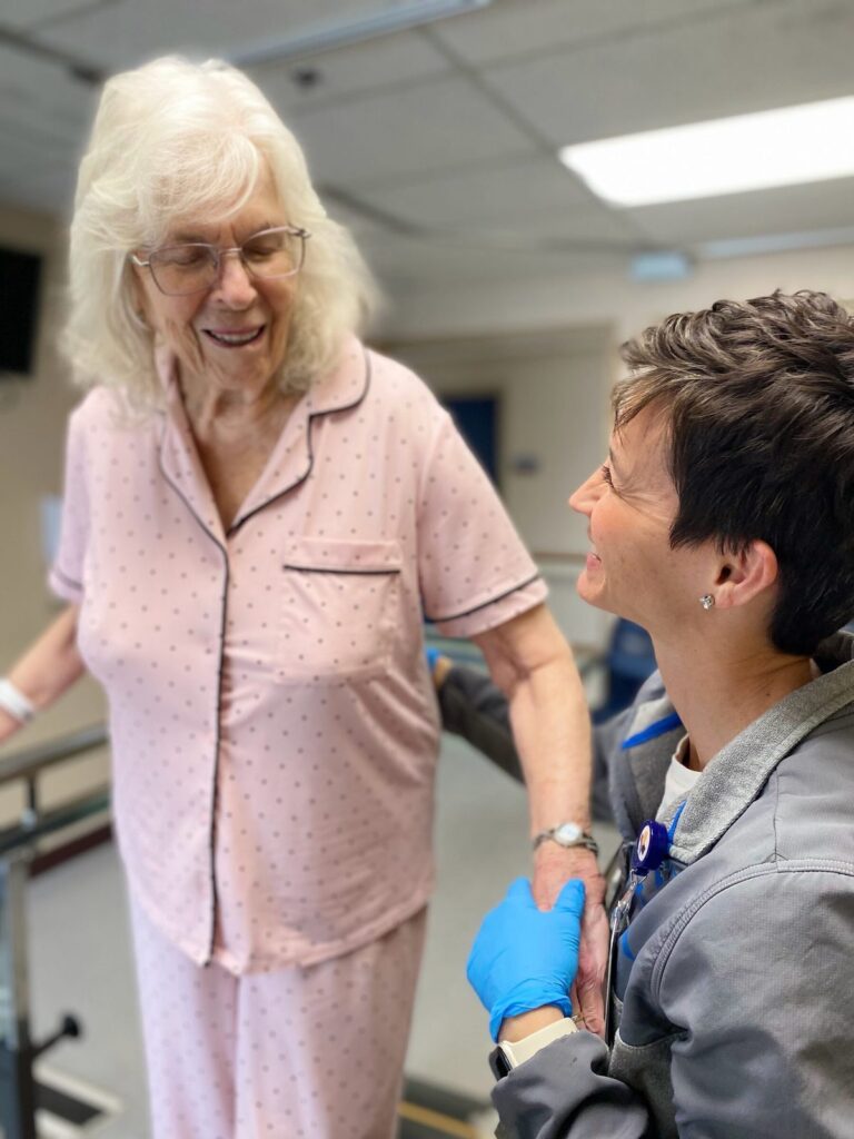 A swing bed patient walks at the parallel bars with her therapist