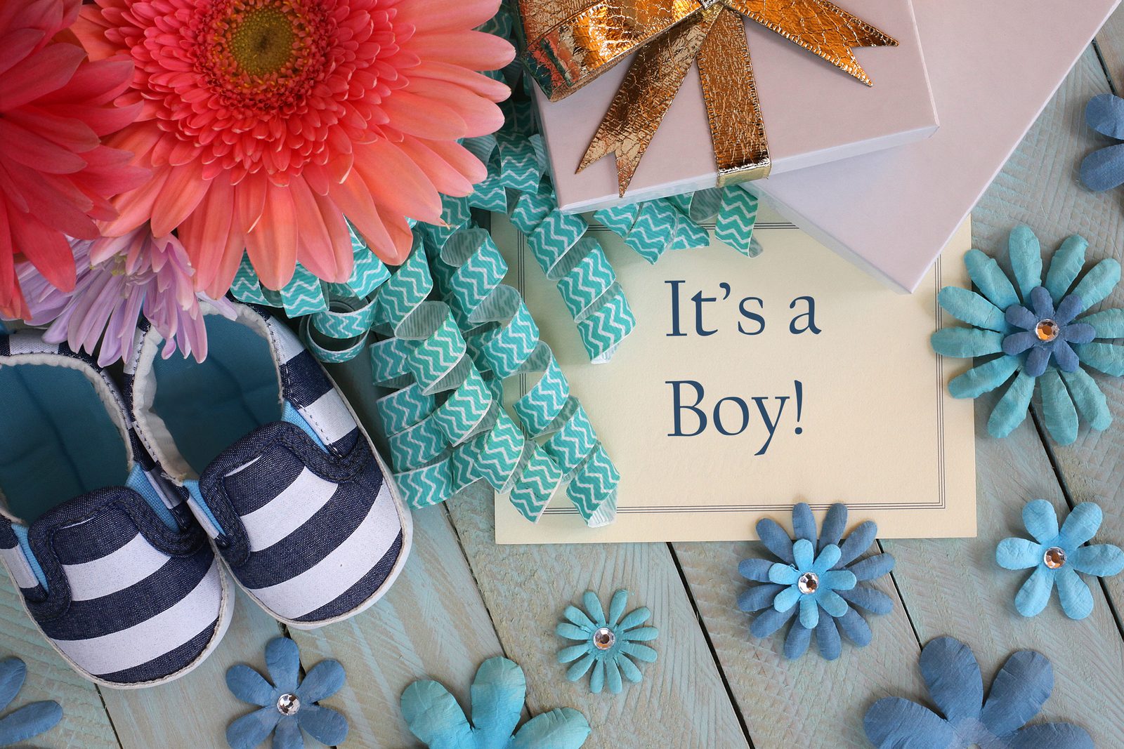 Striped baby shoes, flowers, curling ribbon and gifts around a card that reads It's a Boy!