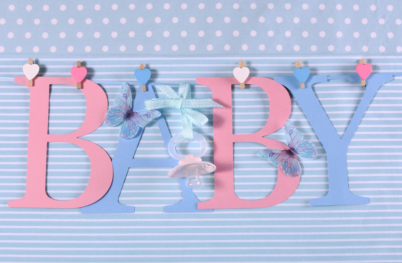 Paper letters spelling BABY in pink and blue, hung with small hearts, with a pacifier and butterflies.